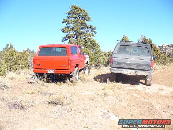 Red and gray Ford Broncos parked on a dirt trail with trees and blue sky