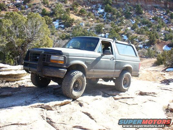 1996 Ford Bronco with bull bar and roof rack driving on rocks
