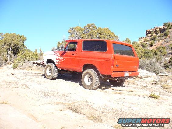 Red and white Ford Bronco with flame decals parked on rocky terrain