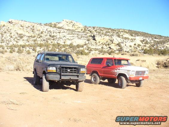Two Ford Broncos parked in a desert. One is red with flames, the other is dark colored