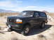 1986 Ford Bronco - A black Ford Bronco is parked in a desert landscape under a clear blue sky.