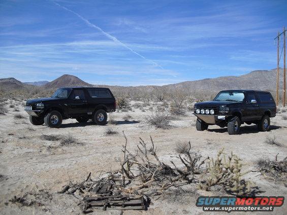 Two black Ford Broncos parked in a desert landscape under a blue sky