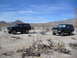 1986 Ford Bronco - Two black Ford Broncos are parked in a dry, desert environment with mountains in the background.
