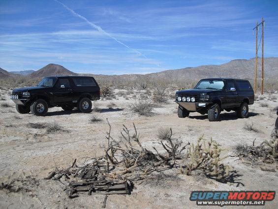 Two black 1987 Ford Broncos parked in a desert with mountains in the background