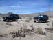 1986 Ford Bronco - Two modified black Ford Broncos are seen in a desert environment under a clear blue sky.