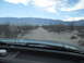 1986 Ford Bronco - View from inside a vehicle driving on a dusty desert road towards distant mountains.