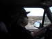 1986 Ford Bronco - A man wearing a camouflage hat drives a vehicle through a barren desert, with mountains in the distance.