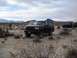 1986 Ford Bronco - Two black Ford Broncos are parked in a desert setting under a cloudy sky.