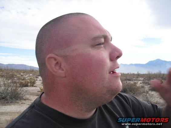Man looking out at a desert landscape with mountains in the background. Supermotors logo visible