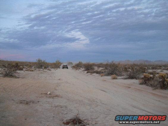 SUV driving on a dirt road in a desert landscape under a cloudy sky