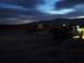 1986 Ford Bronco - A vehicle drives through a desert landscape as the sun sets, its lights illuminating the path ahead.