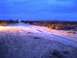 1986 Ford Bronco - Headlights cut through the twilight of a desert landscape, illuminating tire tracks on a dirt road.