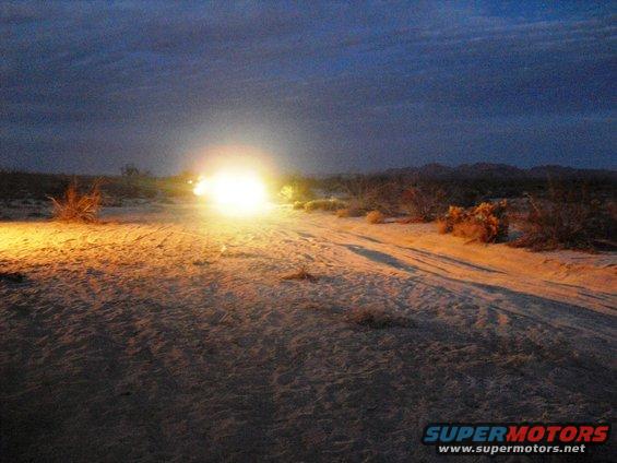 Off-road vehicle with bright headlights on a desert dirt road at dusk