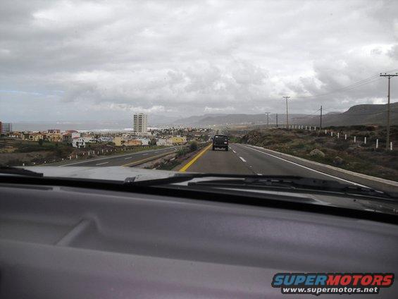 Black SUV on highway with coastal town in background