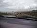 1986 Ford Bronco - A black SUV travels down a highway towards a coastal town under a cloudy sky.