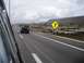 1986 Ford Bronco - A black SUV travels down a highway under a cloudy sky, with a yellow directional sign visible on the right.