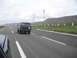 1986 Ford Bronco - A black SUV travels down a highway under an overcast sky, with another vehicle in the foreground.
