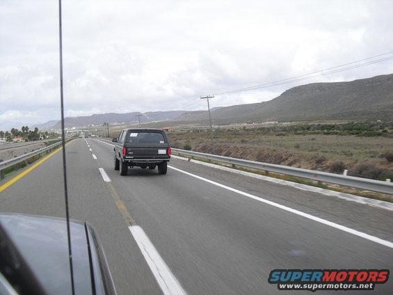 Black SUV from the rear, driving on a highway with mountains in the background