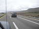 1986 Ford Bronco - A black SUV travels down a highway under a cloudy sky, with a mountainous landscape visible in the distance.