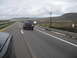 1986 Ford Bronco - A black Ford Bronco from the 1980s is seen from behind while driving on a highway under a cloudy sky.