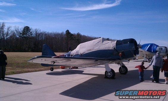 Two airplanes parked on tarmac, one with a grey cover, under a blue sky