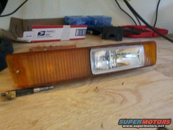 amber plastic turn signal assembly with clear lens and bulb, lying on a wooden surface