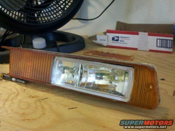 Headlight assembly with amber turn signal and dual bulbs on a wooden surface