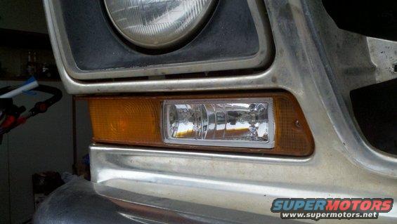 Close-up of a vehicle's front corner, showing the headlight, amber turn signal, and a clear fog light