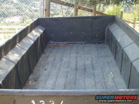 Interior of a truck bed with ribbed floor and angled sides. Some debris is visible