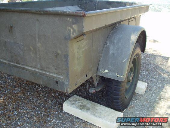 Olive drab military trailer side view, resting on concrete blocks