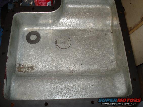 Close-up of a metal oil pan with a gasket. There's a circular indentation with a '9' inside