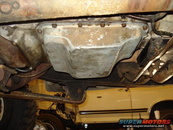 Transmission pan on a vehicle underside, with exhaust pipe and part of a yellow vehicle visible below