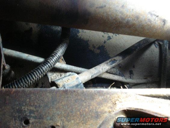 Undercarriage view showing rusted frame, hoses, and wiring conduit