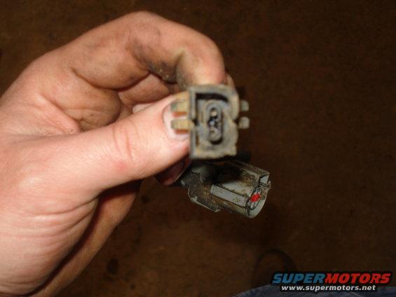 Hand holding two dirty electrical connectors, one with three pins visible
