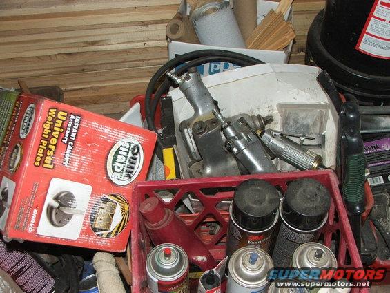 Red crate filled with automotive tools and parts, including spray cans and air tools