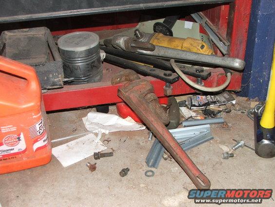Orange cleaner jug, red pipe wrench, and various tools on a concrete floor