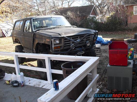 Dark brown 1980s Ford Bronco with aftermarket bumper and winch, missing front fenders and hood, lifted suspension