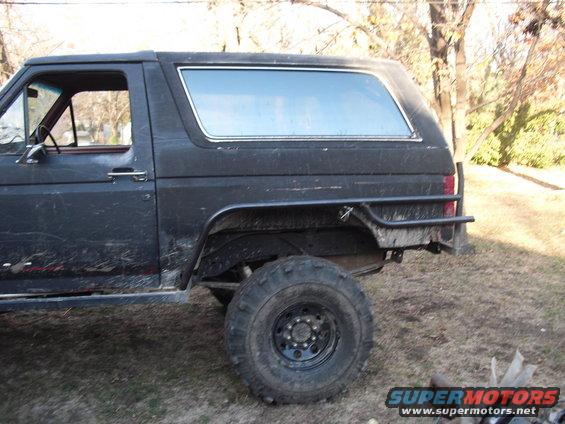 Side view of a dark-colored Ford Bronco with off-road tires and a roll bar over the rear fender