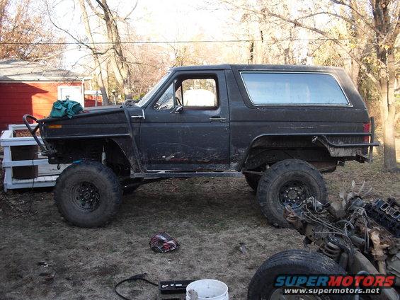 Black SUV with large tires and custom bumpers, parked outside with a disassembled engine in the foreground