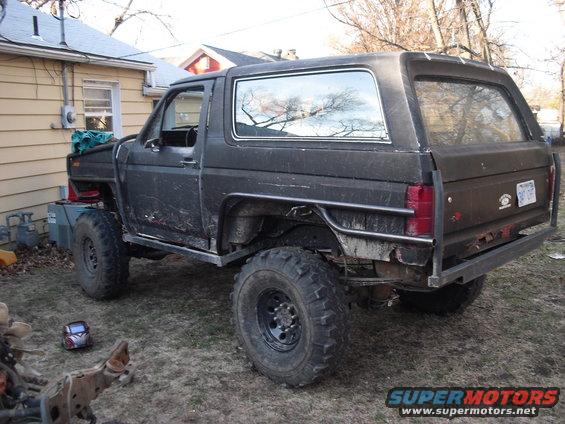 Black SUV with off-road tires and roll cage, rear 3/4 view