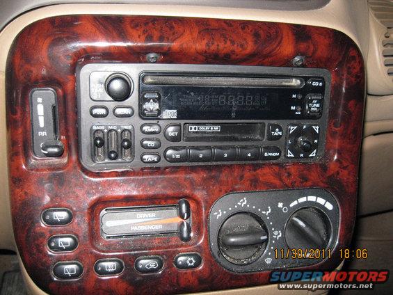 Close-up of a car's dashboard showing a wood-grain trim around the radio, climate controls, and various buttons