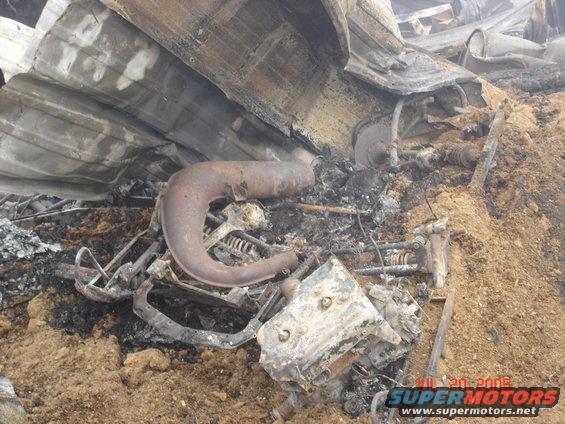 Burnt snowmobile engine and exhaust pipe amidst debris and dirt