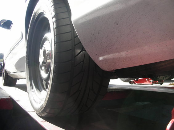 Close-up of a car's rear tire and fender, with a red jack visible underneath