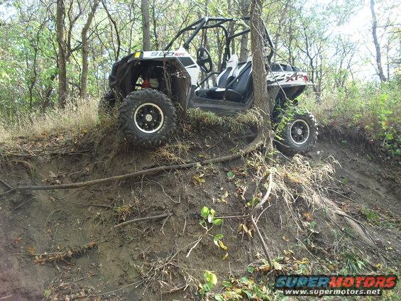 White and black side-by-side off-road vehicle on a muddy embankment with trees