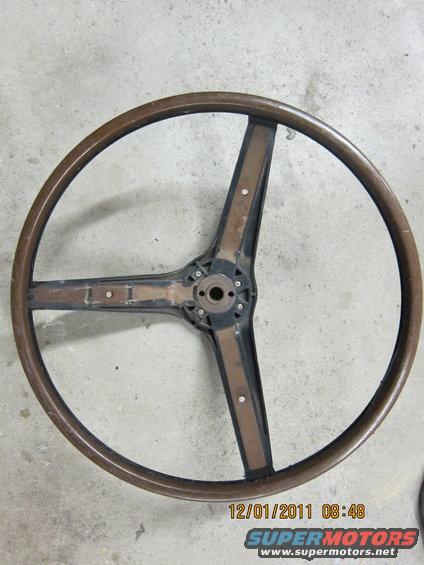 Wooden steering wheel with three spokes and a central hub, lying on a concrete surface