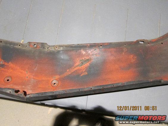 Close-up of a rusty, orange-painted metal piece with holes along the edge