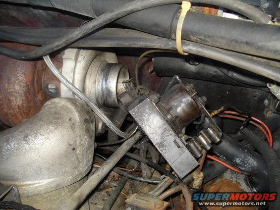 Engine bay with turbocharger, hoses, and electrical connectors. Rusty metal visible