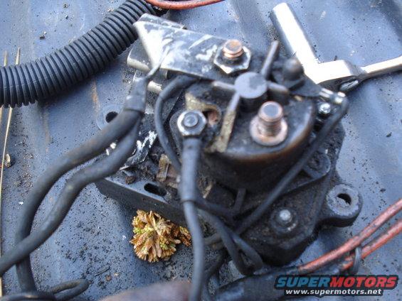 Dirty starter solenoid with copper terminals and black wires attached, resting on a dark surface