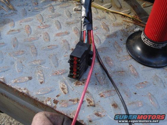 Close-up of a black wiring harness connector with red and black wires, resting on a diamond plate surface
