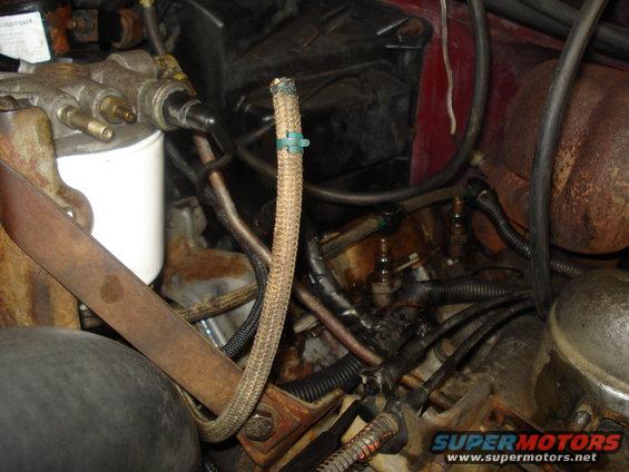 Engine bay showing a white fuel filter, braided hose with a green clip, and various wires and metal components